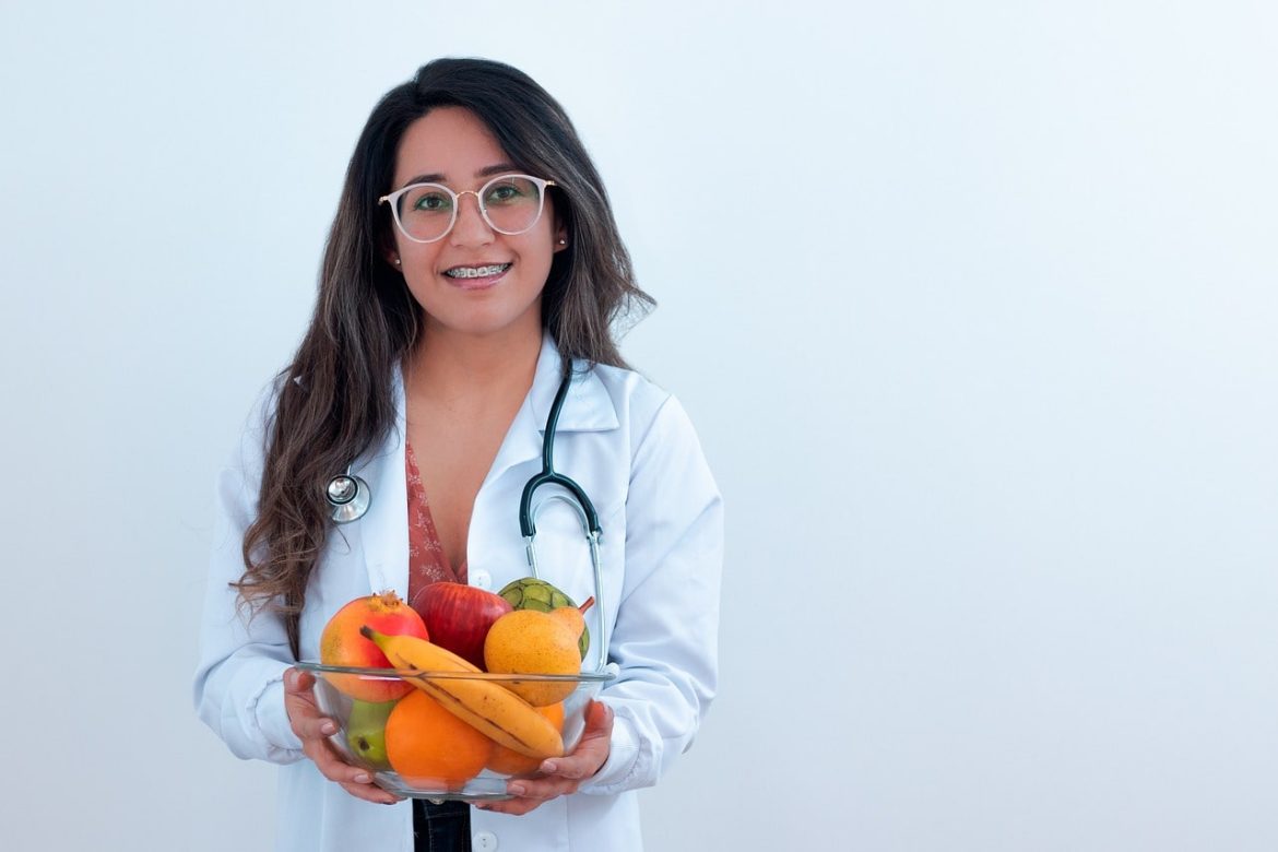 Formation en nutrition : les fruits pour la santé. Jeune femme médecin souriante tenant un bol de fruits frais, concept de formation en nutrition.