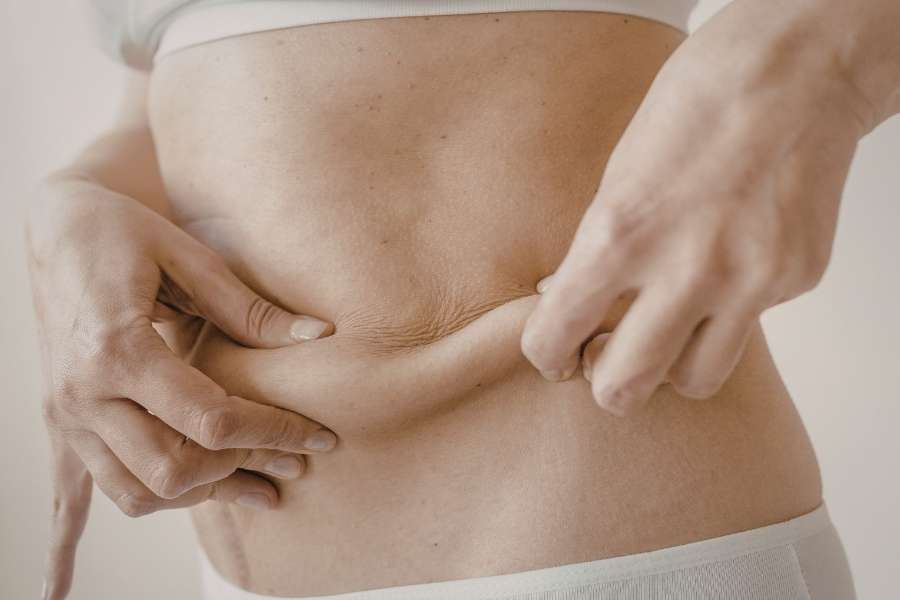 Une femme pince la peau de son ventre pour visualiser la graisse abdominale avant de maigrir du ventre.