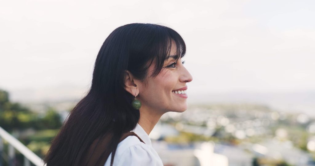 Femme souriante de profil regardant vers l'avenir, symbole d'une évolution personnelle réussie en plein air.