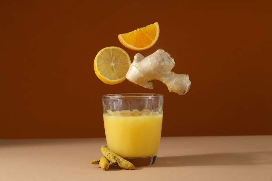 Un verre de jus frais entouré de gingembre, de curcuma et de tranches d'agrumes en lévitation, symbolisant l'approche naturelle de l'oligothérapie.