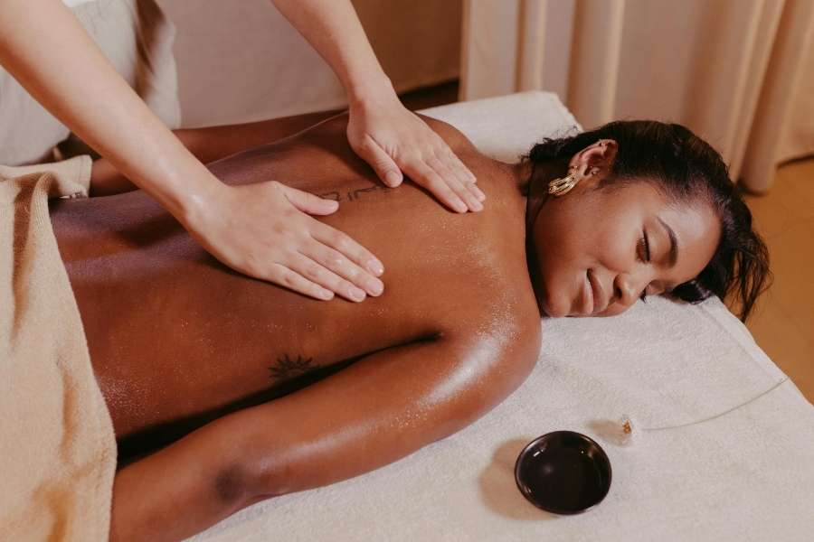 Une masseuse effectue un massage relaxant du dos sur une femme noire souriante dans un spa.